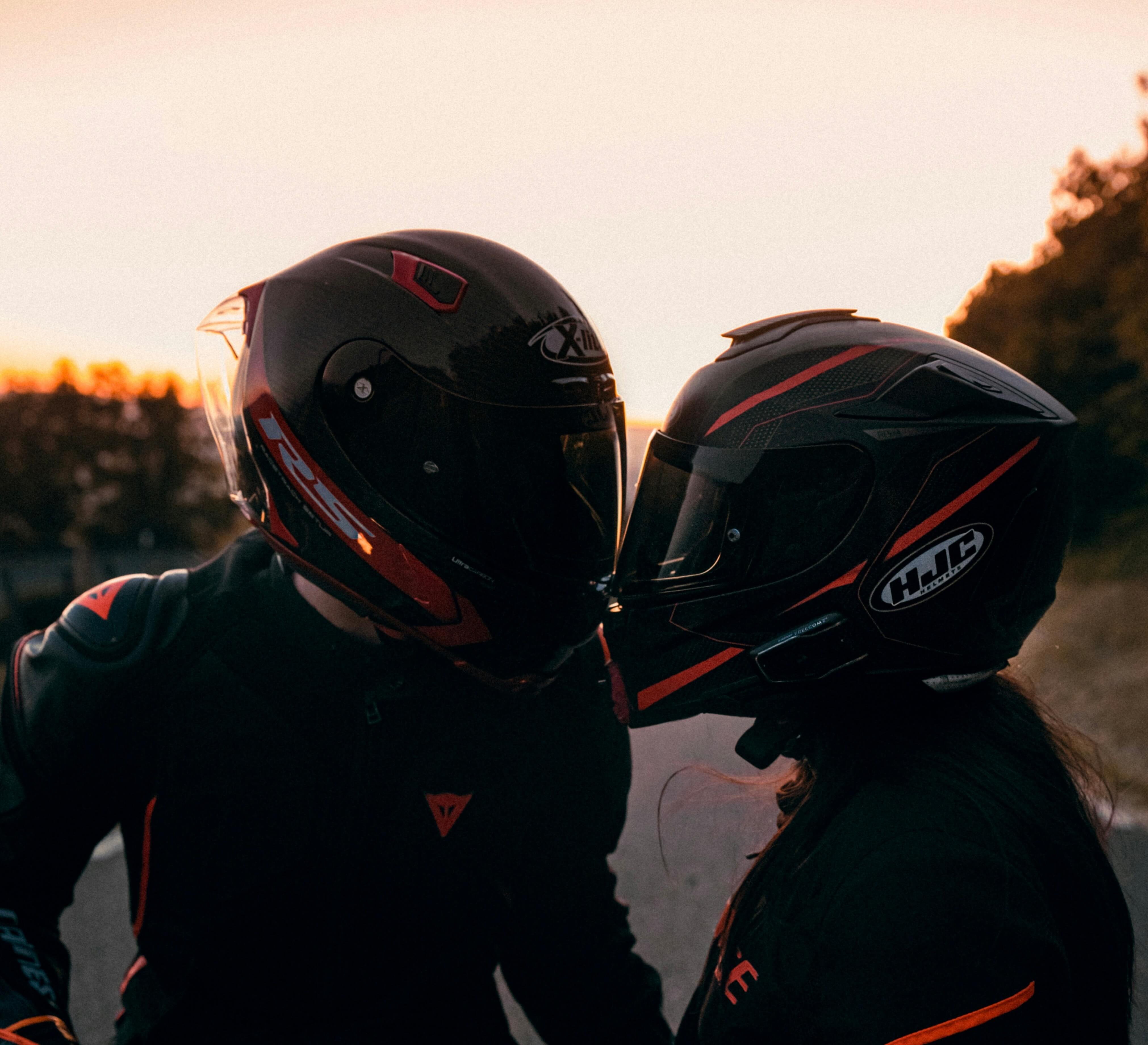 Two people in motorcycle helmets hugging.